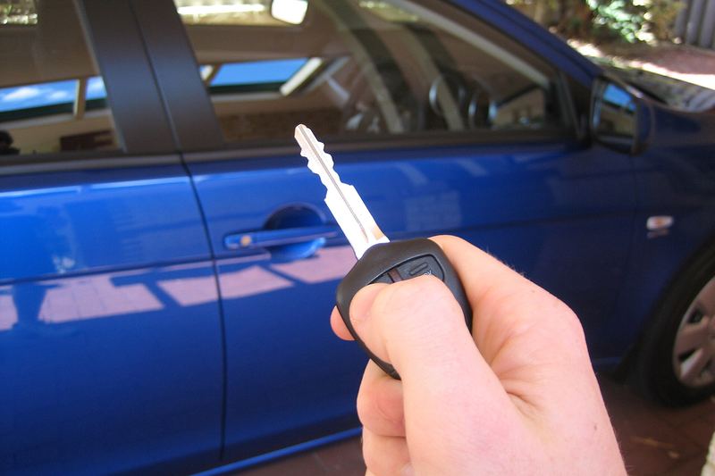 Hand using a remote car key next to a car
